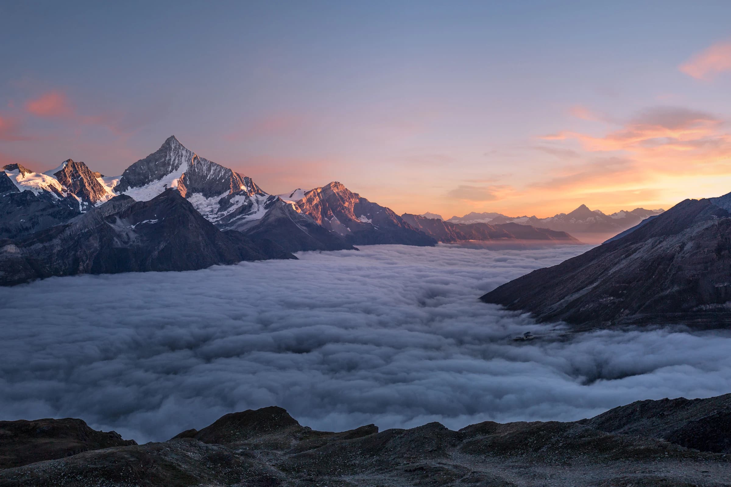 Cime nevose che sorgono sopra un mare di nuvole nella luce tardo pomeriggio