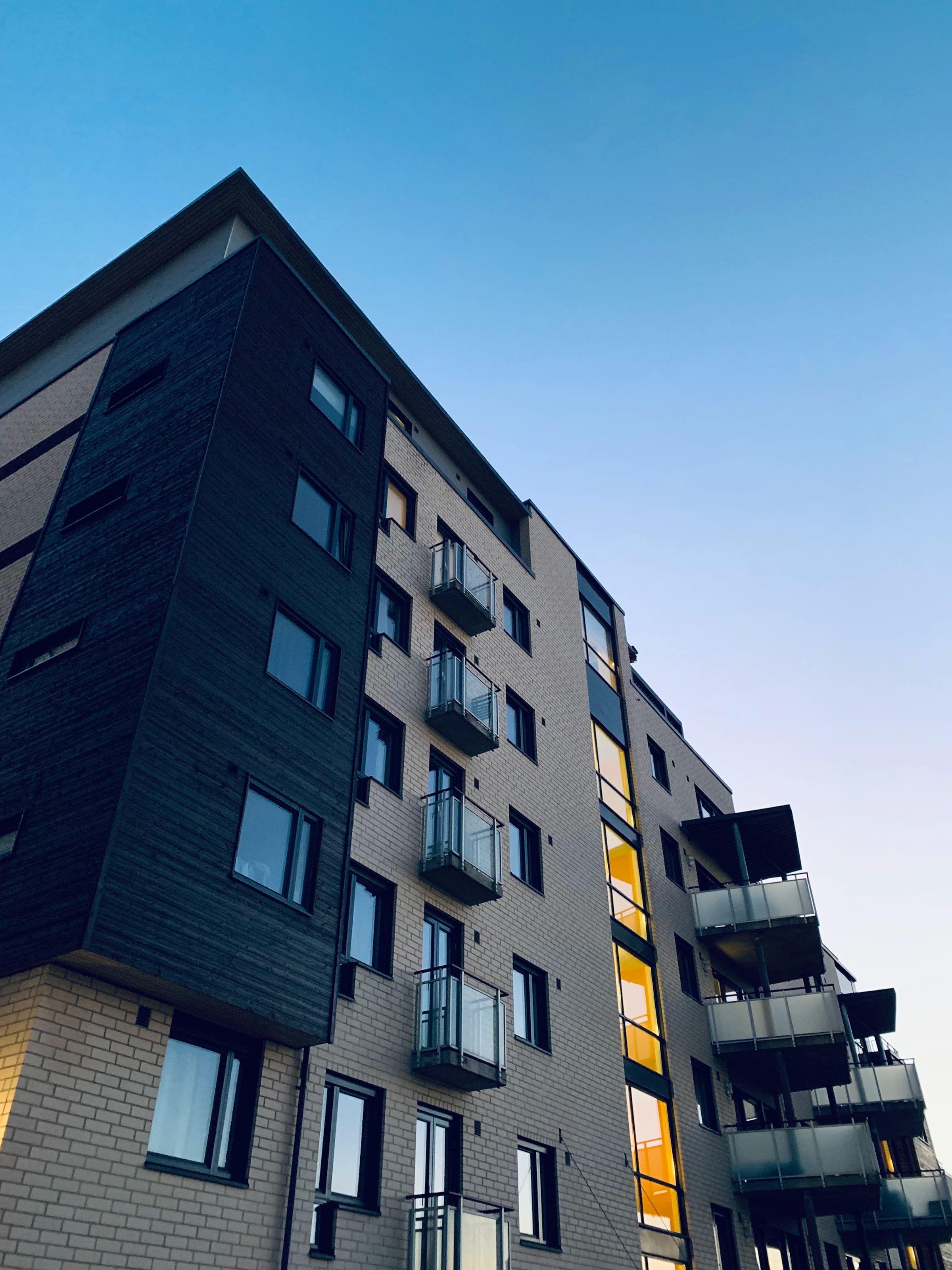 Facade of residential building with balconies on tape and glass reflecting the blue sky