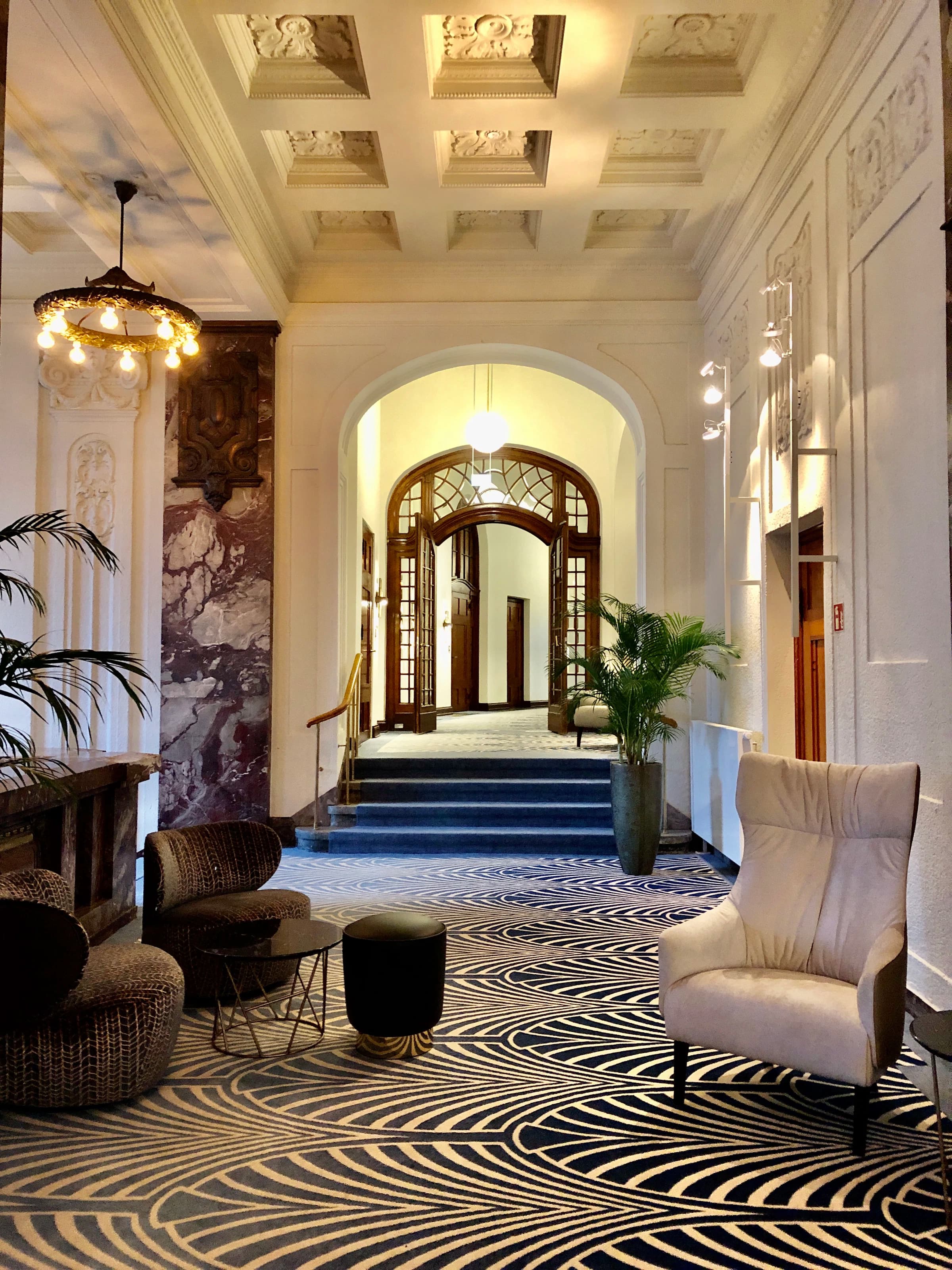 Hotel lobby with marble columns, arch door, palm trees and armchairs