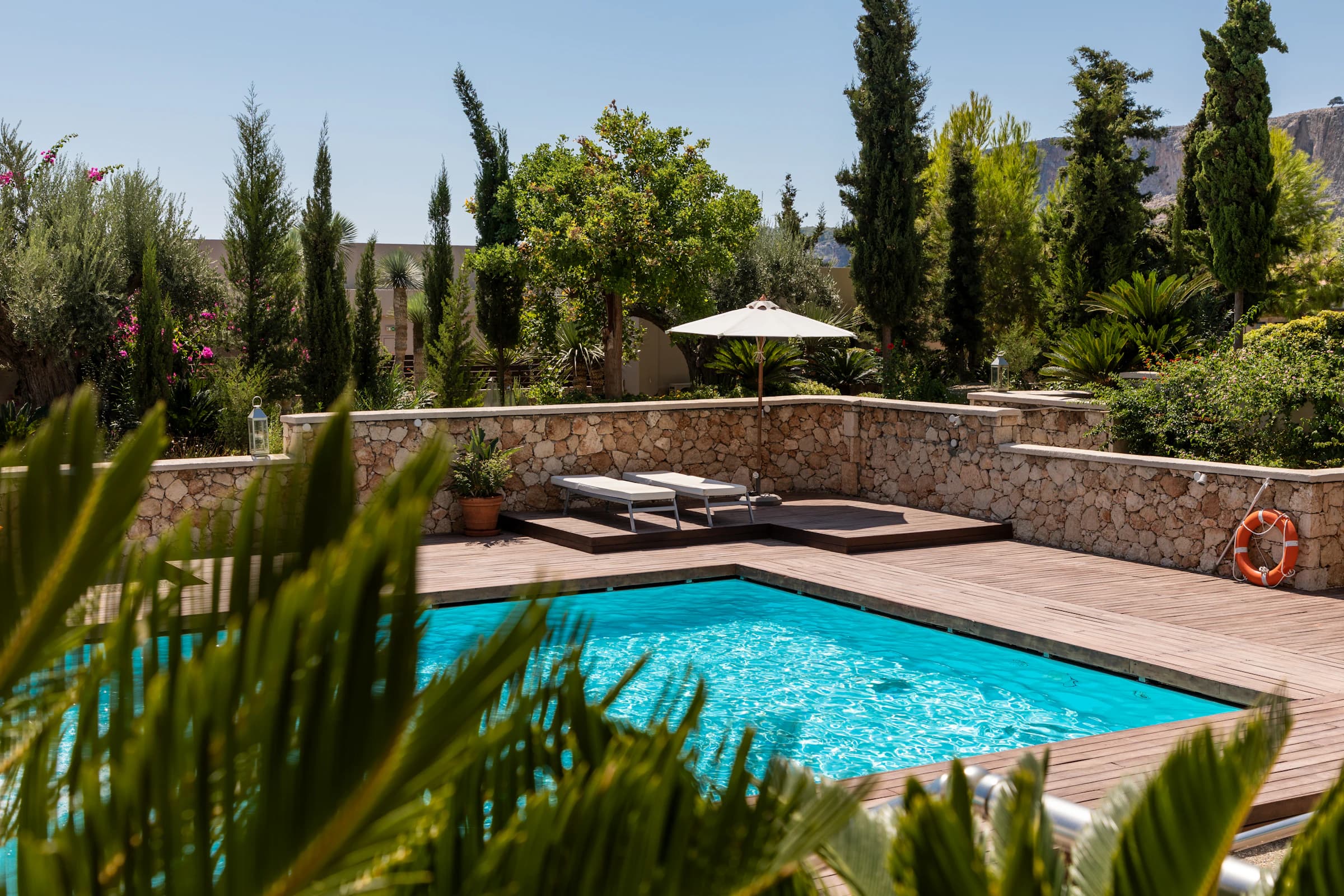 Mediterranean villa pool with stone wall, cypresses and parasol