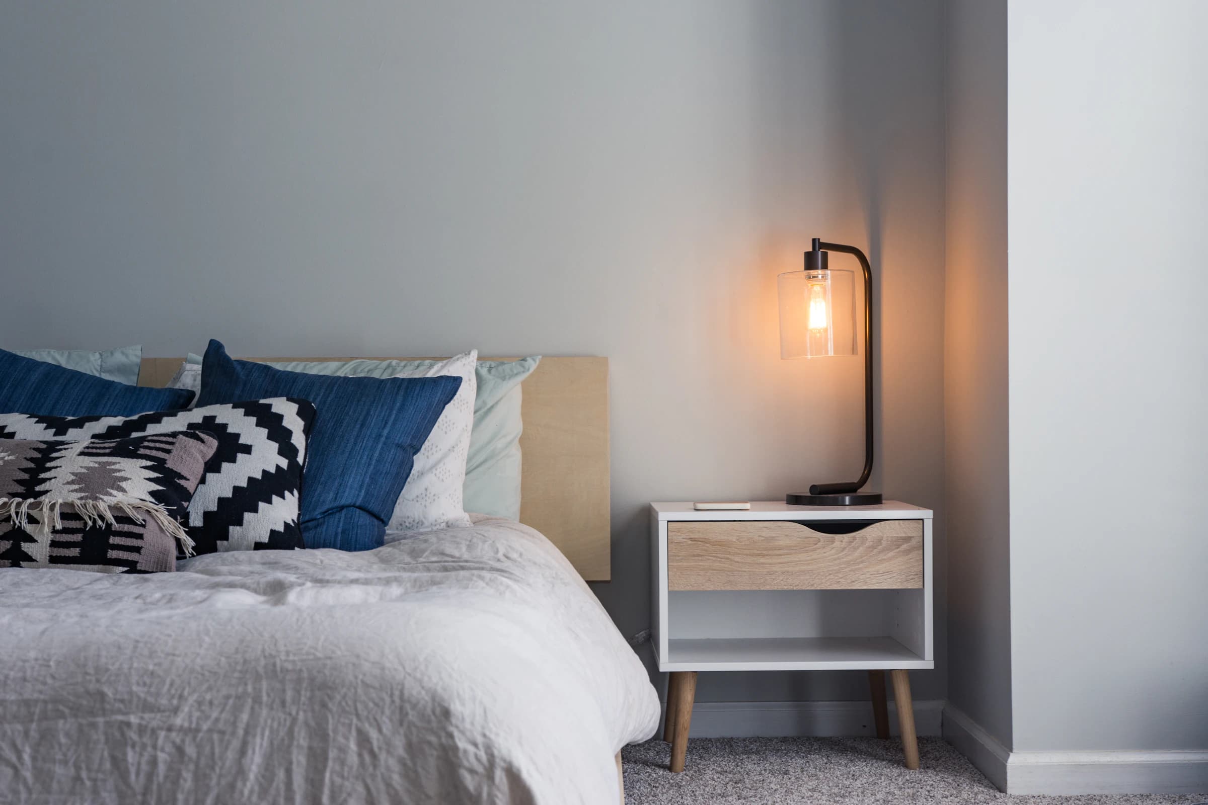 Double bed with white bed linen, piled cushions and light lamp on the bedside table