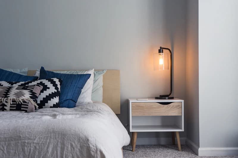 Double bed with white bed linen, piled cushions and light lamp on the bedside table