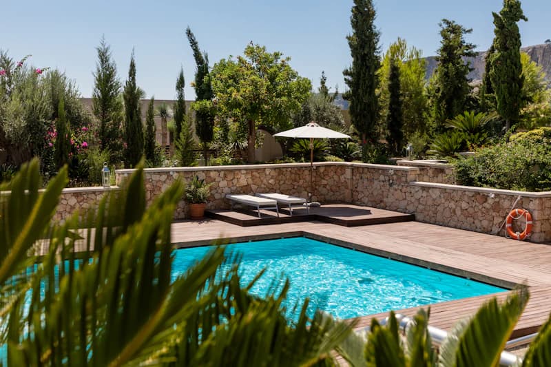 Mediterranean villa pool with stone wall, cypresses and parasol