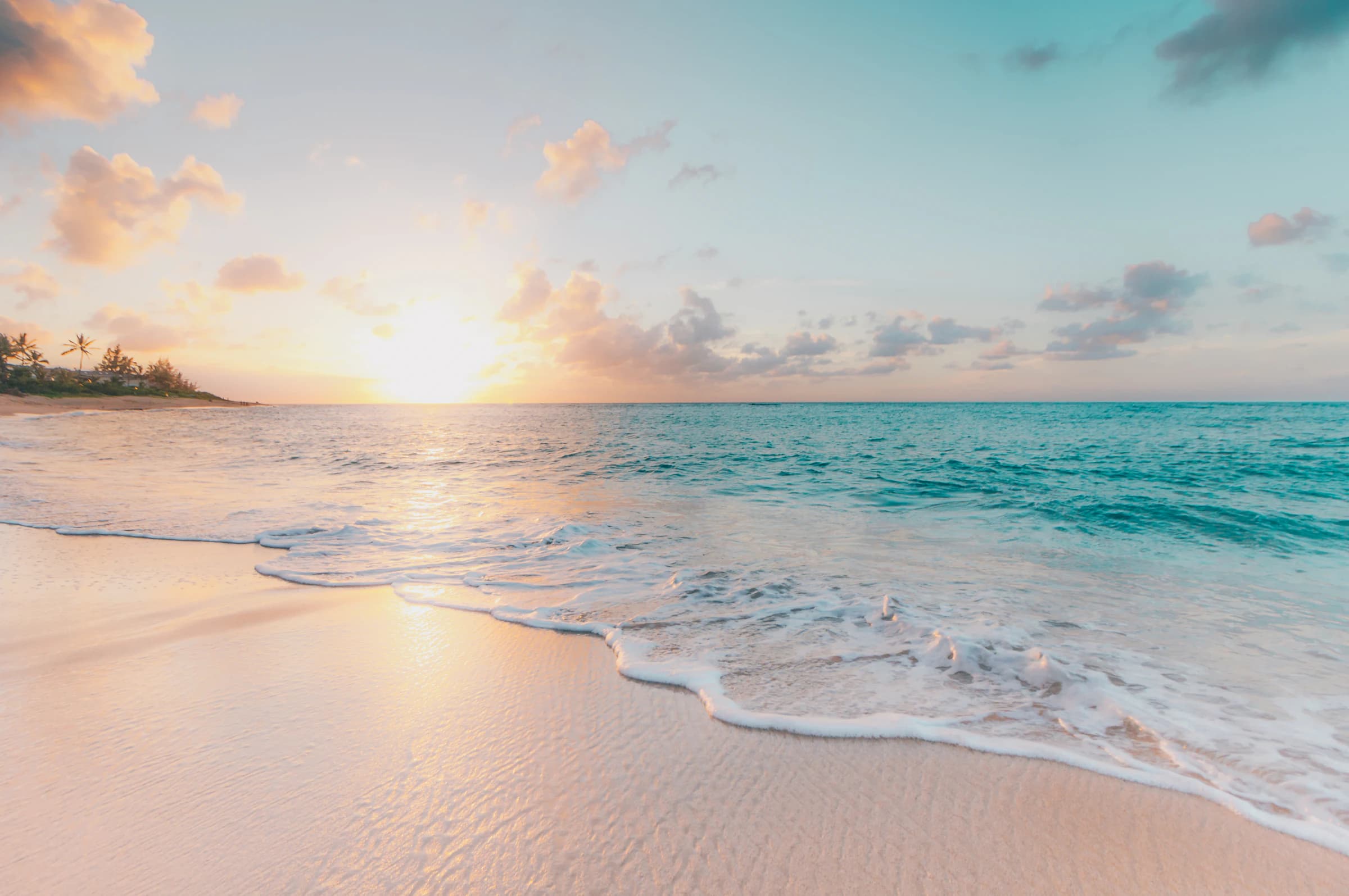 Beach of light sand and turquoise water among dark rocks, with the calm sea at the bottom